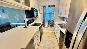 A compact kitchen with white cabinets, a stainless steel refrigerator, a microwave, and a stove.