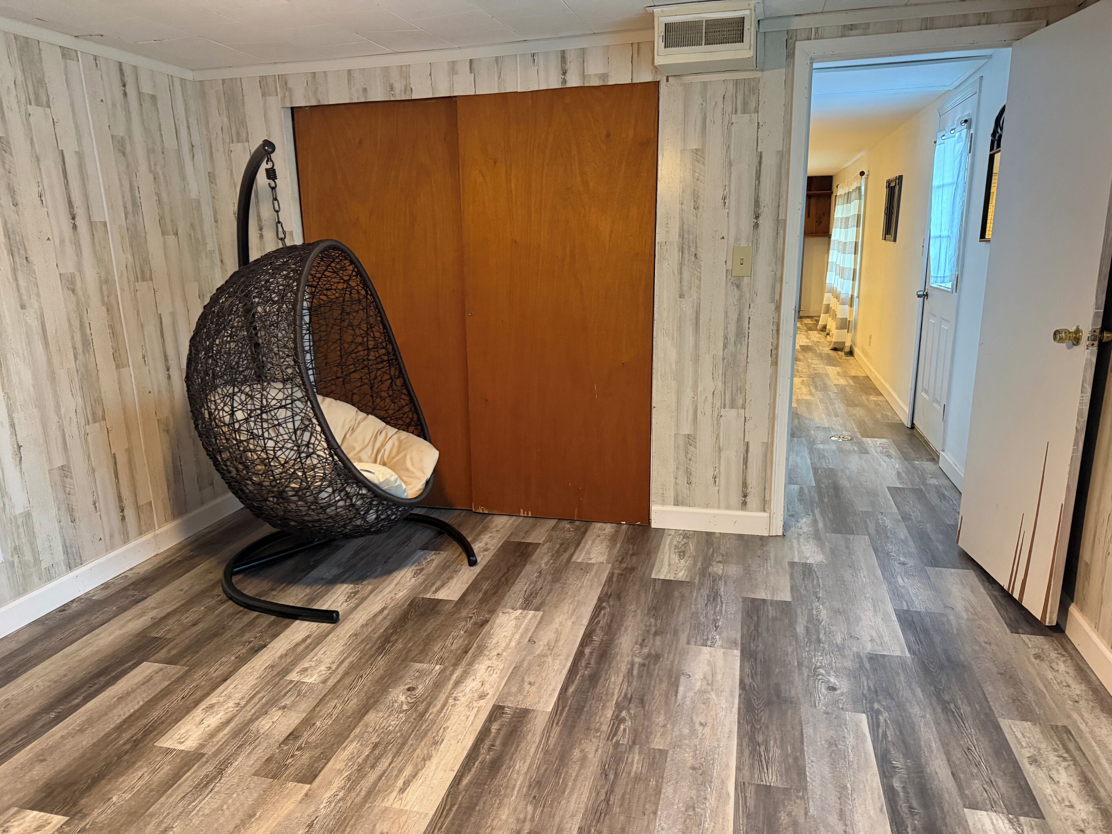 Une pièce dotée d’un fauteuil suspendu, d’un plancher en bois, d’une porte coulissante et d’un couloir menant à une autre pièce.