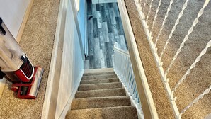 A carpeted staircase with a handrail, a red object on the left, and a patterned wall in the background.