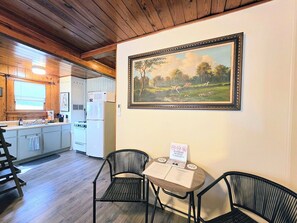 A kitchen with wooden cabinets, a microwave, a refrigerator, and a sink. There is a framed painting on the wall and a table with chairs. - Willow Whisper Cottage (Hot Springs)