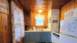 A compact kitchen with wooden walls, a sink, a stove, and a refrigerator. - Wildflower's Escape (Hot Springs)