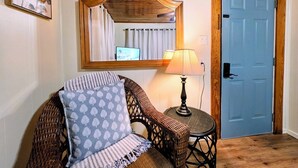 A room with a wicker chair, a lamp, a mirror, and a blue door. - Wildflower's Escape (Hot Springs)