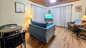 A cozy living room with a wooden ceiling, a television, a sofa, a dining table, and wicker furniture. - Wildflower's Escape (Hot Springs)