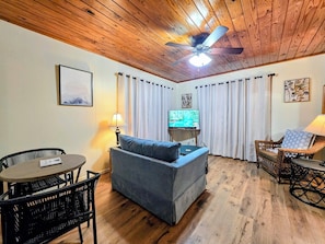 A cozy living room with a wooden ceiling, a television, a sofa, a dining table, and wicker furniture. - Wildflower's Escape (Hot Springs)