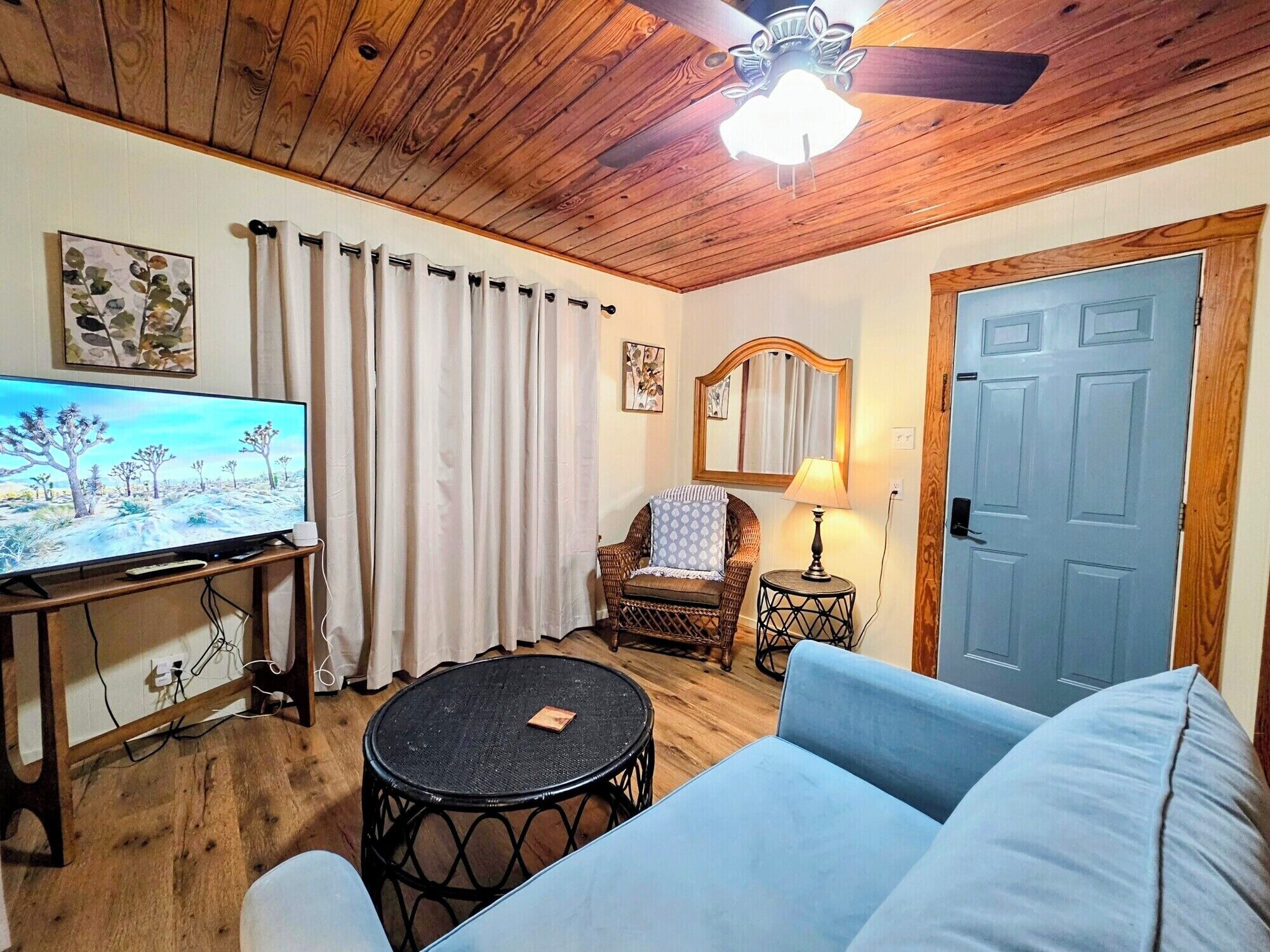 Una sala de estar acogedora con televisor, un sofá, una silla, una mesita redonda y un ventilador de techo.