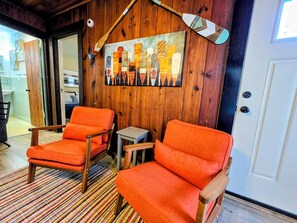 A room with two wooden chairs, a small table, and a colorful abstract painting on the wall. - Paddlers Paradise Cottage (Hot Springs)