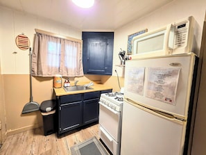 A compact kitchen with a stove, sink, and a refrigerator with a menu. - Paddlers Paradise Cottage (Hot Springs)