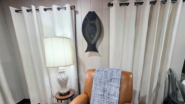 Una habitación con un sillón de cuero marrón, una mesita redonda con una lámpara y un adorno en forma de pez colgado en la pared.