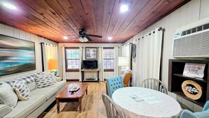 Una sala de estar acogedora con techo de madera, un sofá, una mesa de centro, un televisor y un comedor con mesa y sillas.