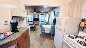 Cocina compacta con estufa a gas, microondas y refrigerador. Hay una mesa de comedor con sillas y un televisor pequeño montado en la pared.
