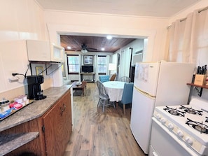 A compact kitchen with a gas stove, a microwave, and a refrigerator. There is a dining table with chairs and a small TV mounted on the wall. - Heron's Nest Cottage (Hot Springs)