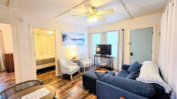 A compact living space with a bed, two chairs, a sofa, a television, and a dining table.