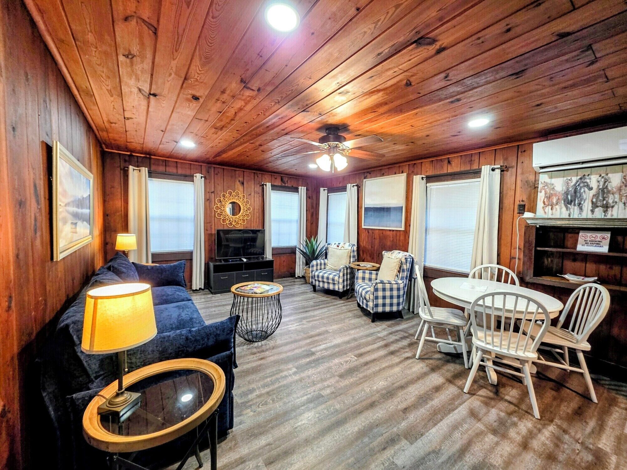Un acogedor interior de cabaña con un sofá, una mesa de comedor con sillas, un televisor y una chimenea.