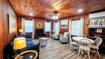 Un acogedor interior de cabaña con un sofá, una mesa de comedor con sillas, un televisor y una chimenea.