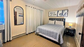 A bedroom with a bed, a mirror, a ceiling fan, a sign on the wall, and a window with curtains. - Pebble Beach Cottage (Hot Springs)