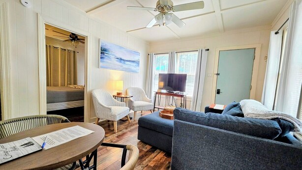 A room with a ceiling fan, a television, a dining table with a menu, a sofa, and a chair. - Serenity Shores Cottage (Hot Springs)