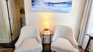 A room with two striped armchairs facing each other, a small table with a lamp, and a large abstract painting on the wall. - Serenity Shores Cottage (Hot Springs)