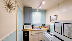 A compact kitchen with a microwave, sink, and stove. - Serenity Shores Cottage (Hot Springs)