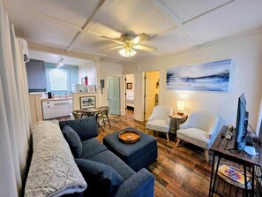 A living room with a sofa, ottoman, and armchairs, a dining area with a table and chairs, a kitchen with a microwave, and a ceiling fan. - Serenity Shores Cottage (Hot Springs)