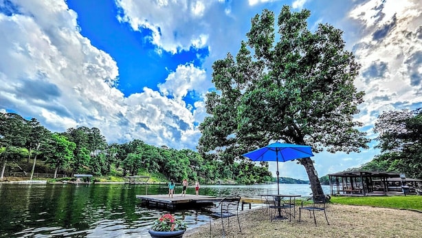 Un parco sul lago con un molo, tavoli da picnic e un ombrello blu.