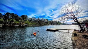 Un lago tranquillo con un kayak, un molo e un albero sulla destra.