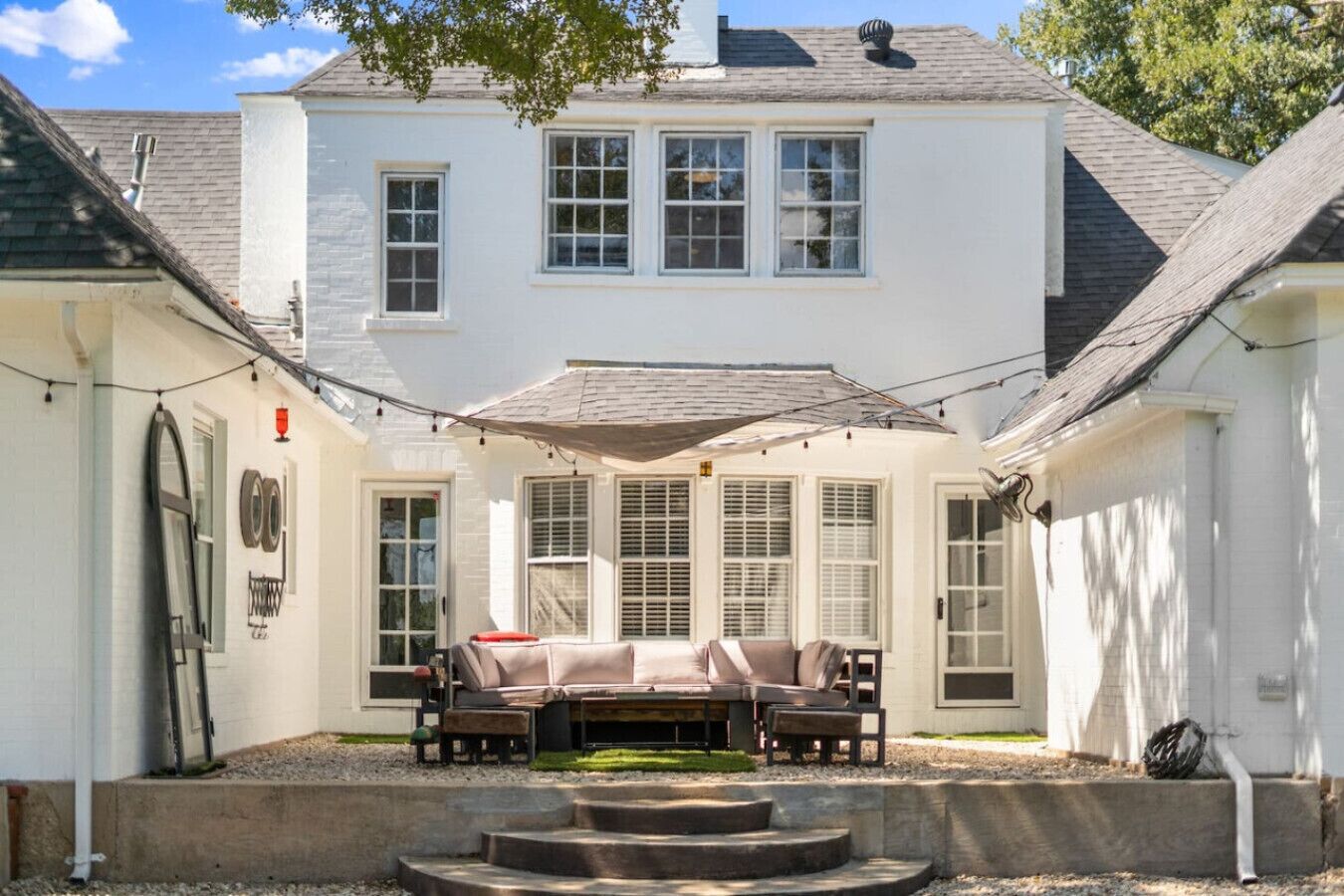 A white house with a covered patio, a set of steps leading to the entrance, and a small garden area.