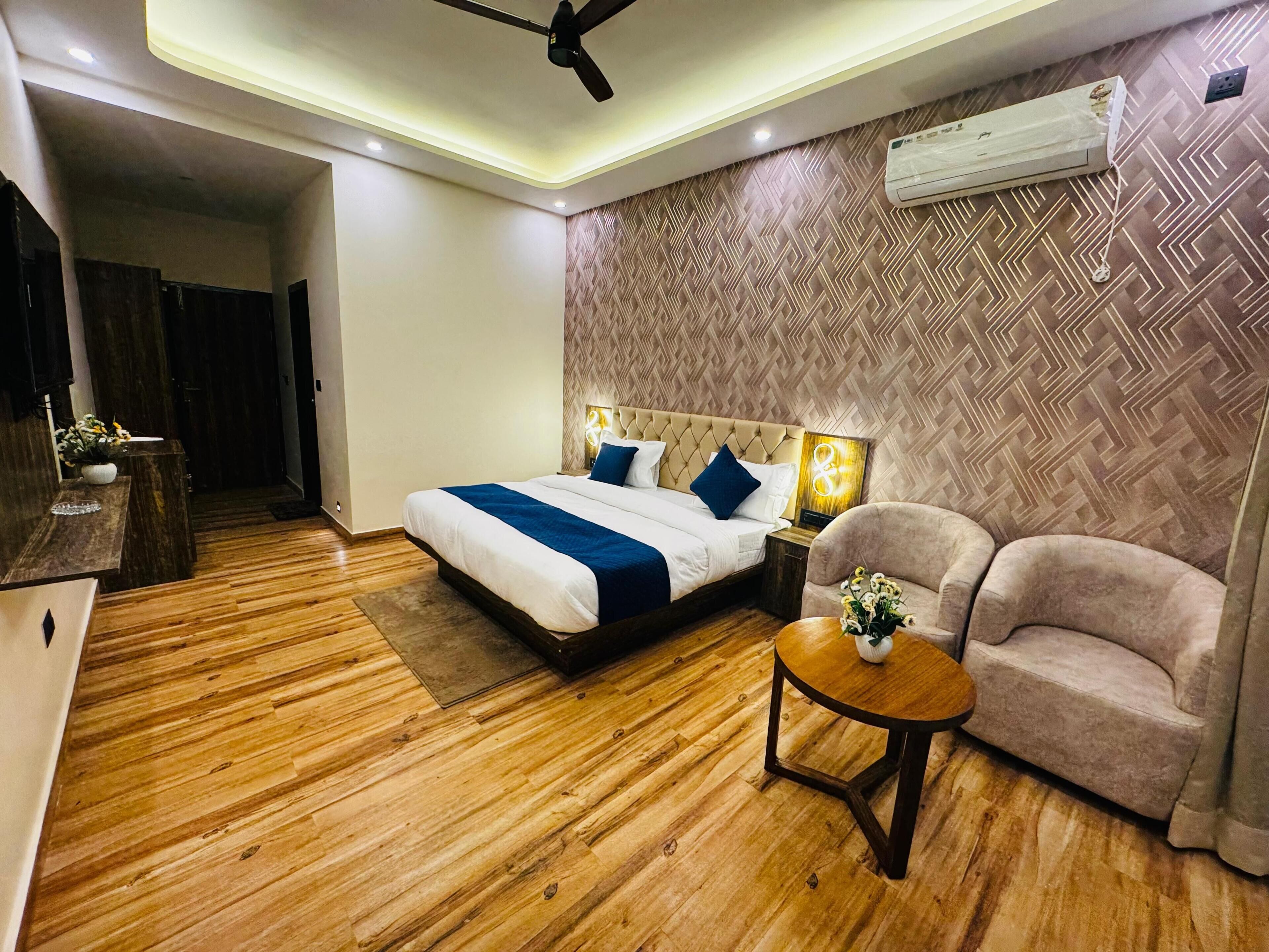 A hotel room with a bed, a desk, a chair, a round table, and an air conditioning unit.