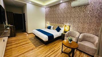 A hotel room with a bed, a desk, a chair, a round table, and an air conditioning unit.