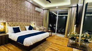 Habitación de hotel moderna con una cama grande, ventilador de techo, televisor y balcón con mobiliario exterior.