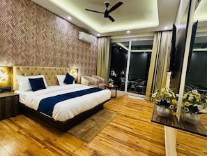 A modern bedroom with a large bed, a ceiling fan, a TV, and a balcony with outdoor seating. - Casa Del Sol Lakeview Homestay (Bhimtal)