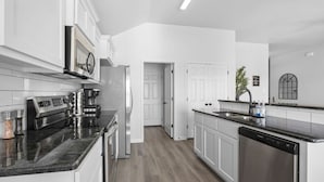 A modern kitchen with white cabinetry, a built-in oven, a microwave, a coffee maker, and a dishwasher. - Brand-New Med District Home (Temple)