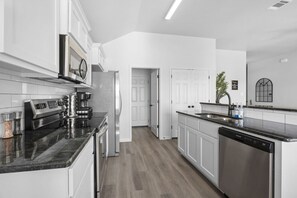 Eine moderne Küche mit weißen Schränken, einem eingebauten Backofen, einer Mikrowelle, einer Kaffeemaschine und einem Geschirrspüler.
