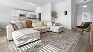 A modern living room with a sectional sofa, a patterned rug, and a ceiling fan. - Brand-New Med District Home (Temple)