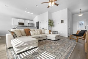 Ein modernes Wohnzimmer mit einem Ecksofa, einem gemusterten Teppich und einem Deckenventilator.