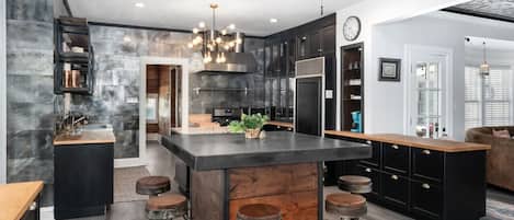 A modern kitchen with a central island, bar stools, and a ceiling fan.
