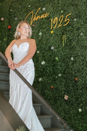 Eine Person in einem weißen Kleid steht auf einer Treppe vor einem grünen Wandhintergrund.