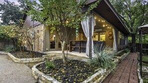 A modern building with a covered outdoor seating area, a brick pathway, and landscaped garden beds. - Triple C Retreat + Pool & Spa (Temple)