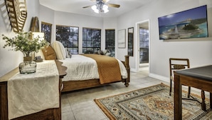 A bedroom with a bed, a ceiling fan, a window with blinds, a painting, and a dining table with chairs. - Triple C Retreat + Pool & Spa (Temple)