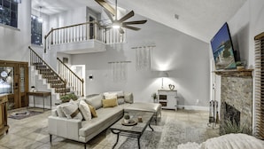A spacious living room with a high ceiling, a staircase, a fireplace, and a large window. - Triple C Retreat + Pool & Spa (Temple)