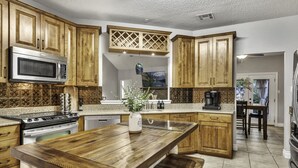A kitchen with wooden cabinets, a central island, a microwave, stove, and a coffee maker. - Triple C Retreat + Pool & Spa (Temple)