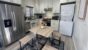 A modern kitchen with stainless steel appliances, white cabinetry, a wooden table, and a patterned rug. - Huntington Beach 2bed/2bath house.| Near Beach, Dining, Family Fun & Relaxation (Huntington Beach)