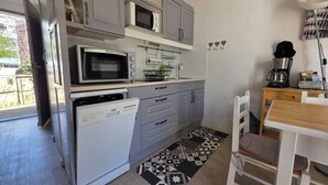 Een compacte keuken met een vaatwasser, magnetron en oven. Er is een klein eethoekje met een tafel en stoelen.