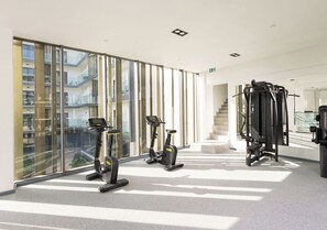 Ein modernes Fitnessstudio mit Cardiogeräten, Kurzhanteln und einer Treppe zu einer oberen Ebene.