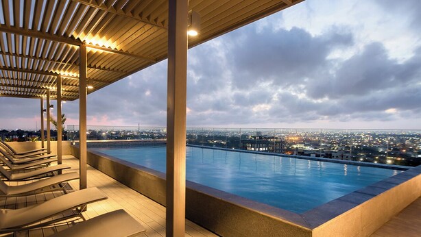 A rooftop pool with lounge chairs, a pergola, and a city view at dusk. - One Bedroom Apartment at The Lennox (Accra)