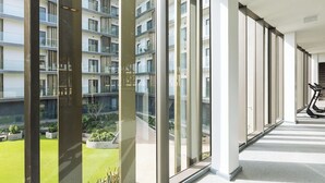 A corridor with large windows, a view of a residential building, and exercise equipment. - One Bedroom Apartment at The Lennox (Accra)