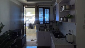A compact kitchen with a stove, sink, and cabinets, a small stool, and a window with curtains.