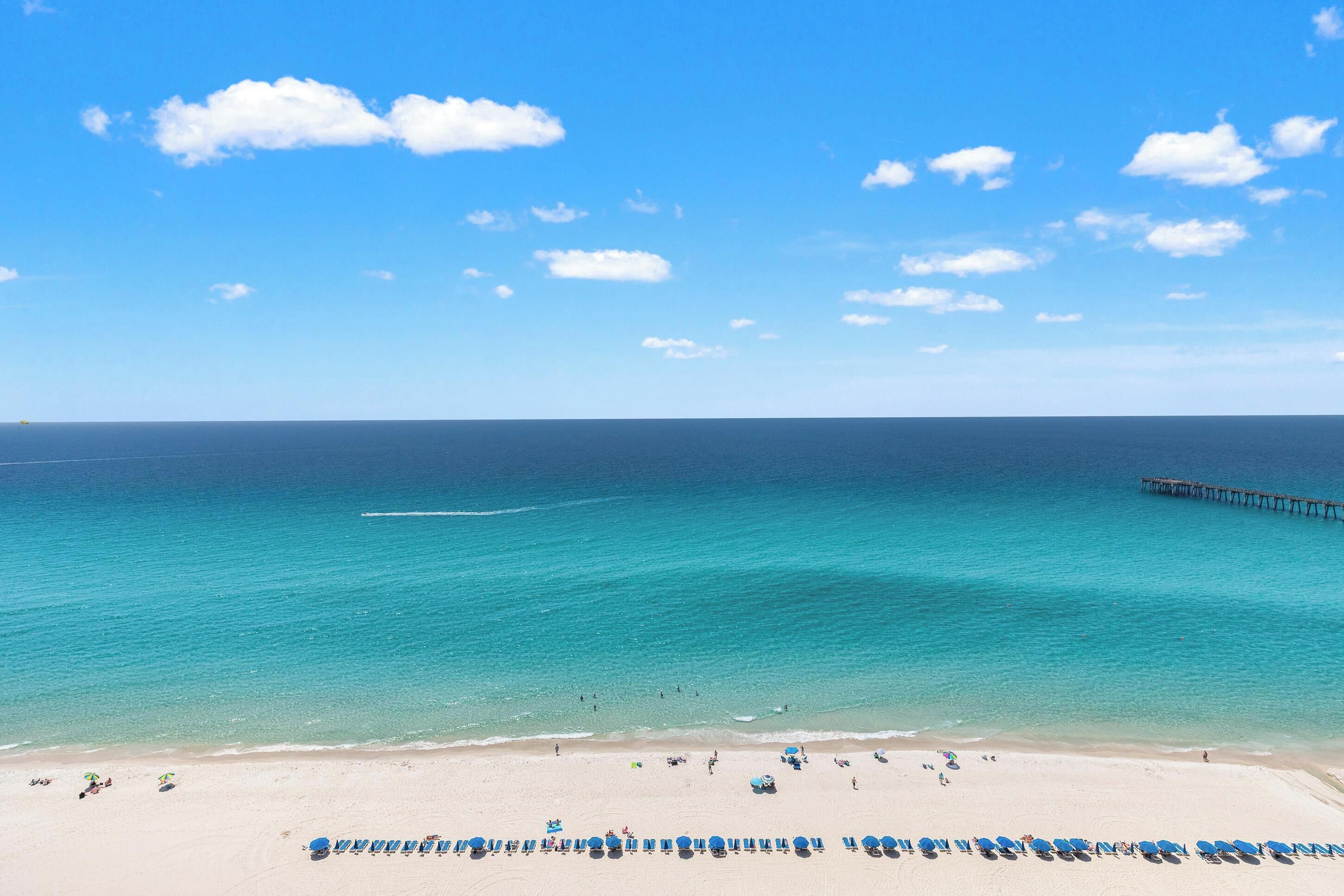 A beach with clear turquoise water, a pier, and rows of beach umbrellas.