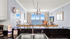 Una cocina moderna con una isla grande, lavamanos de acero inoxidable y vista al océano.