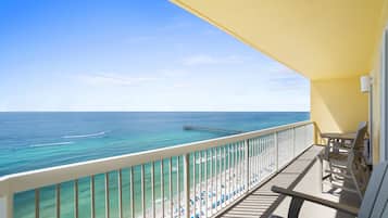 A balcony with a view of the ocean and beach, wooden furniture, and a yellow awning.