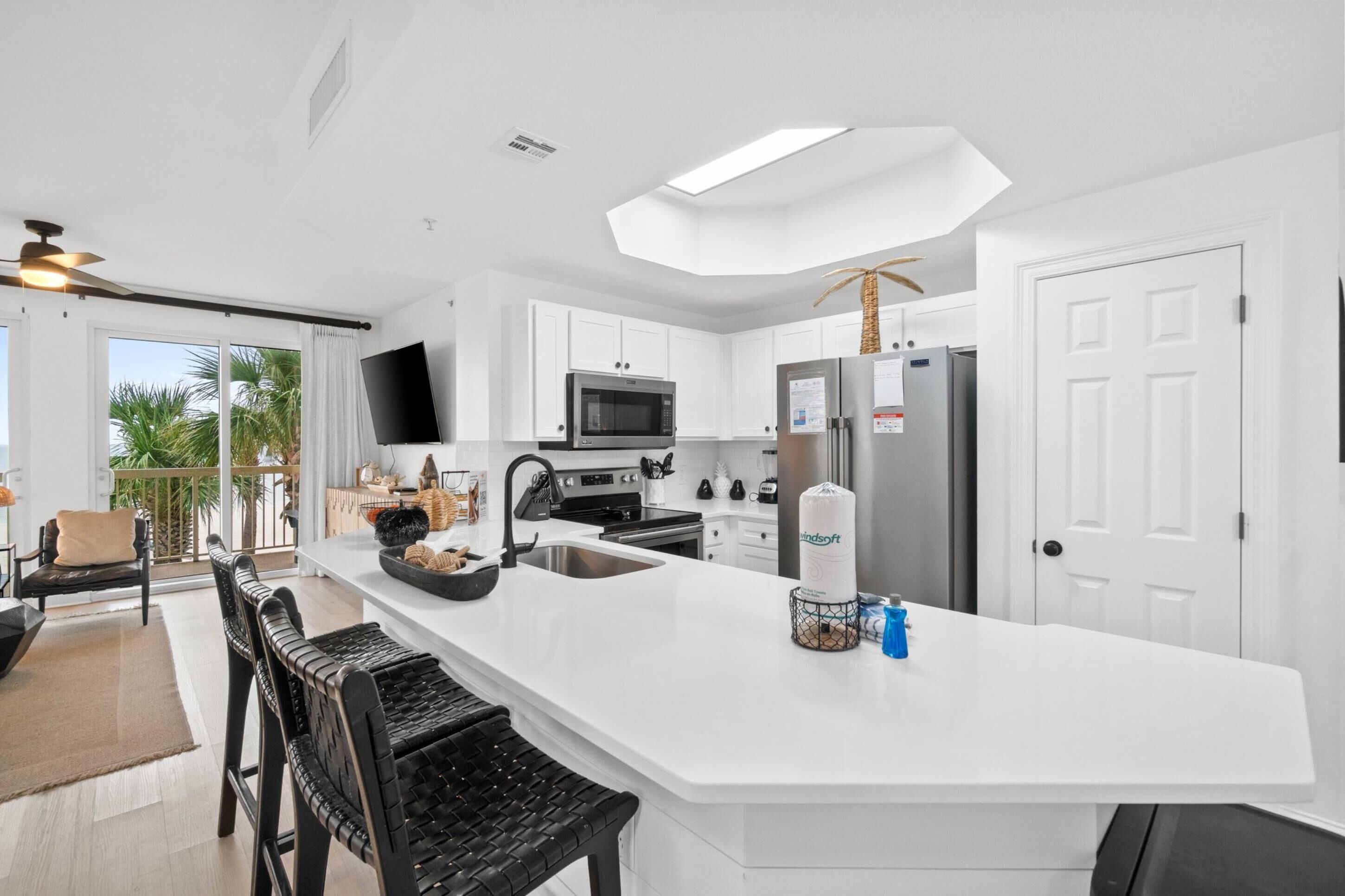 A modern kitchen with white cabinetry, a large island, stainless steel appliances, and a flat-screen TV.